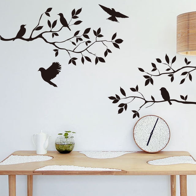 Dvkptbk Wall Stickers Tree Bird Removable Wall Sticker Vinyl Art Decal Mural Home DIY Decor applied to a smooth white wall above a wooden table. The decal features black silhouettes of tree branches, leaves, and birds in flight or perched, creating a nature-inspired look. Perfect for home décor, dorms, or offices, and suitable for smooth surfaces like walls, doors, or tiles.
