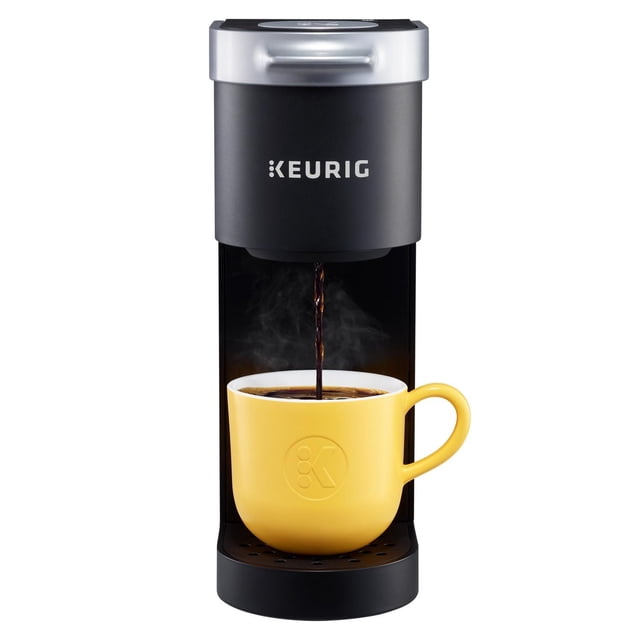 Keurig K-Mini Single Serve K-Cup Pod Coffee Maker in black with silver top, brewing steaming coffee into a yellow ceramic mug embossed with a logo, compact design ideal for small kitchens or offices, compatible with K-Cup pods for quick single-serve coffee.