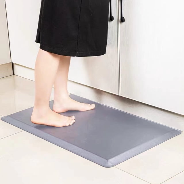 LAKUB Kitchen Mats for Floor, a cushioned anti-fatigue mat in grey, measuring 17x28 inches. The mat is shown placed on a tiled kitchen floor with a person standing barefoot on it. Designed with a non-slip backing, it provides ergonomic support for prolonged standing and features a waterproof, stain-resistant surface for easy cleaning. Suitable for kitchens, laundry rooms, or standing desks.