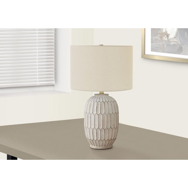 Monarch Specialties Lighting 24"h table lamp with a textured cream resin vase-shaped base featuring a hexagonal pattern, topped with an ivory linen drum shade and gold metal finial, set on a taupe table near a window with white blinds and framed abstract art on a cream wall, ideal for living rooms or bedrooms.