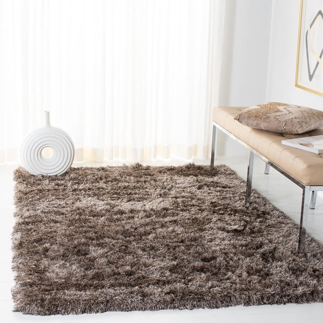 Safavieh Paris Darwin Plush Shag Area Rug in sable, 5 by 7 feet, with a 2.5-inch thick plush shag pile featuring textured depth, placed in a bright room with white sheer curtains, a beige leather bench with metal legs, and a white circular decorative vase, suitable as an accent rug for living rooms or bedrooms.