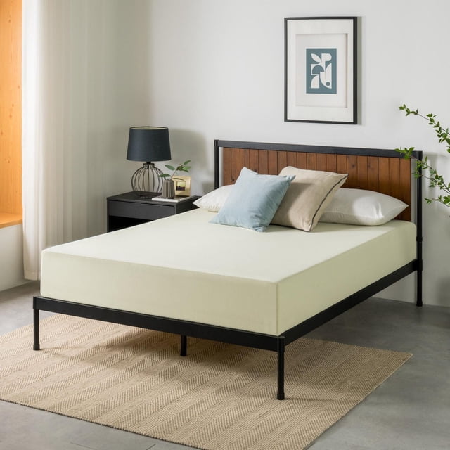 Zinus 10 inch Gel Airflow Memory Foam Mattress, Queen, on a black metal frame with wooden slat headboard in a minimalist bedroom. The mattress has a breathable gel memory foam layer with a smooth cream cover, topped with light blue and beige pillows. The room features a black bedside table with lamp and plant, framed abstract art, and a beige textured rug on concrete floor.