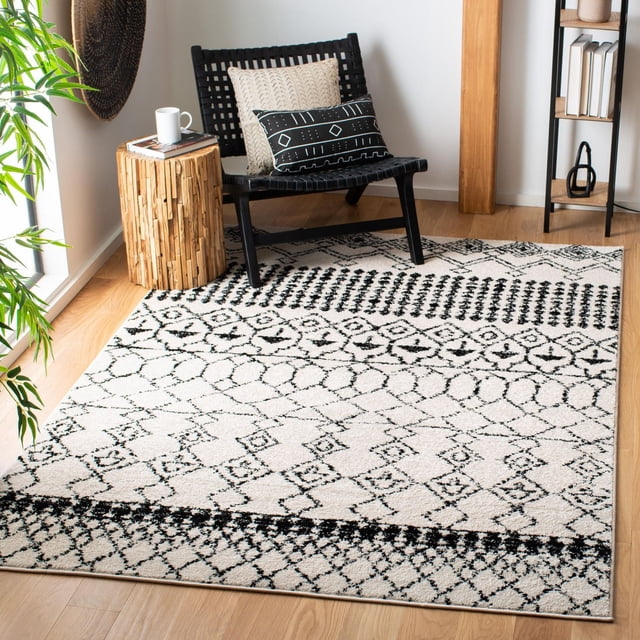 SAFAVIEH Tulum Coriander Moroccan Geometric Area Rug featuring black and white geometric diamond and linear patterns on a plush hand-knotted wool surface, displayed in a bright room with a black woven chair, wooden side table, and decorative pillows, ideal for adding warmth to modern interiors.