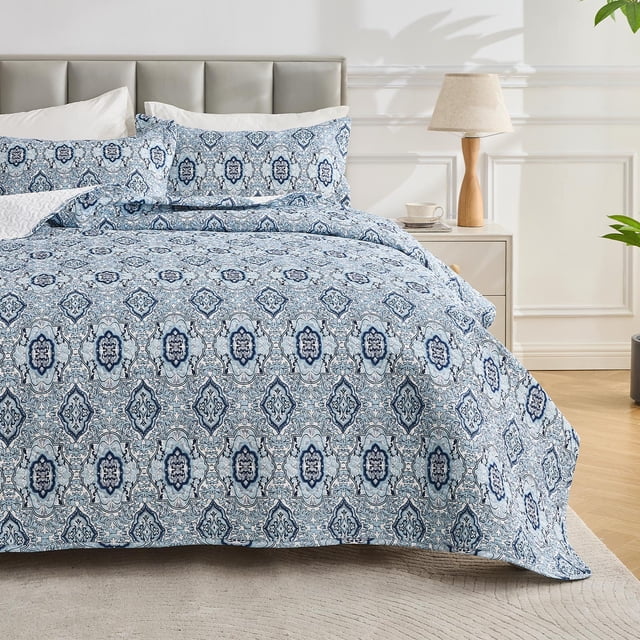 Hitime Luxury Printed Quilt Set Queen Size, a lightweight comforter set with oversized bedspread coverlet, displayed in a bedroom. The quilt showcases elegant floral patterns in blue and white, paired with two matching pillowcases. Crafted from brushed microfiber with heavier-than-average microfiber filling, it ensures softness, durability, and all-season comfort. The bedding is styled on a bed with a grey upholstered headboard, accompanied by a nightstand and decor accents.