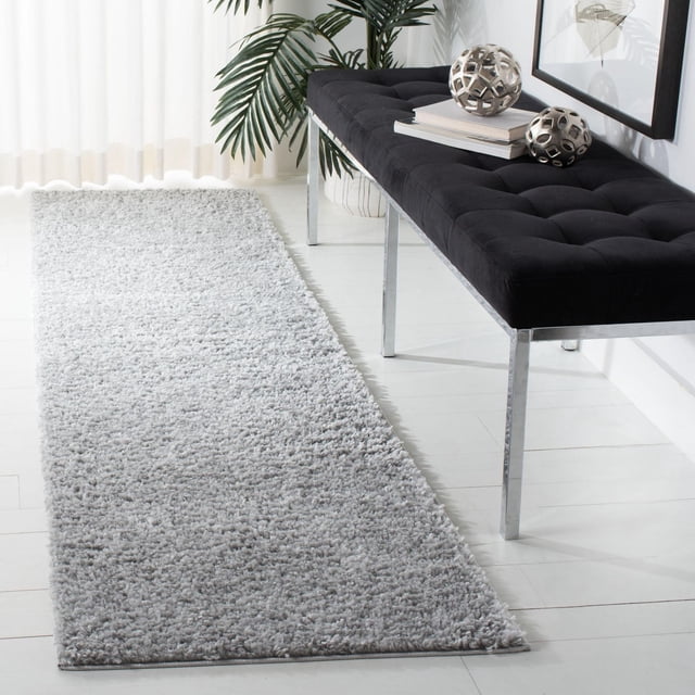 SAFAVIEH August Carlene Tapis Shag Moelleux Uni en Gris Pâle avec une Épaisse pile Shag en Polypropylène, Posé sur un Plancher de Bois Blanc à Côté d'Un Banc Capitonné Noir avec Pattes Chromées. le Tapis Rectangulaire Complète les Intérieurs Décontractés de la Côte Ouest et Convient aux Couloirs Ou aux Entrées.