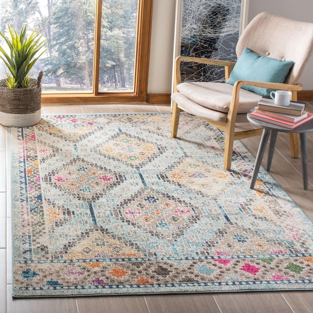 SAFAVIEH Madison Lanford Vintage Geometric Area Rug in beige with blue and pink diamond patterns, power loomed for durability and easy care, shown in a bright room with a beige wooden armchair with a blue cushion, a small round side table with books and a cup, and a woven basket plant near a large window. The rug's transitional style suits contemporary home décor and is often used to add subtle color and texture to living spaces.