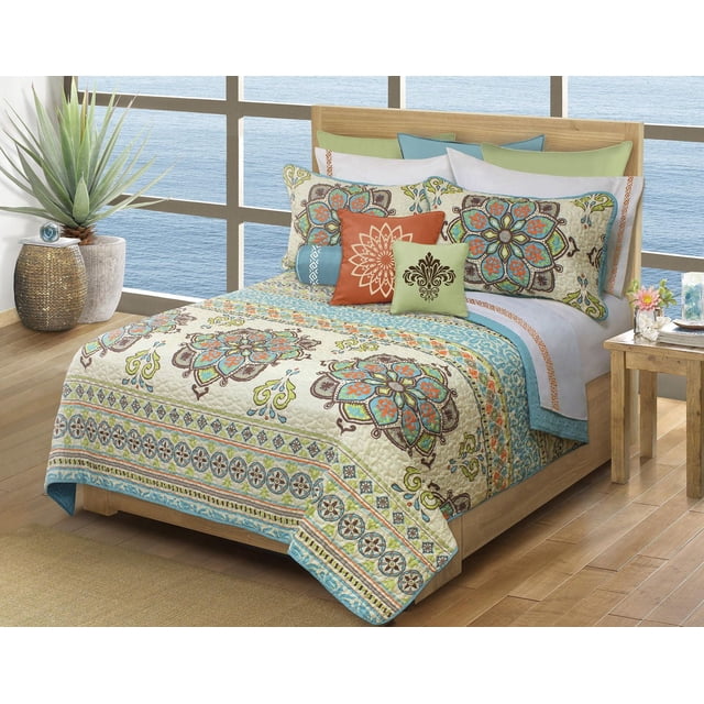 Safdie & Co. Home Deluxe Collection Multi Color 100% Polyester Quilt Set on a twin wooden bed with a printed quilted coverlet and two matching pillow shams featuring floral and geometric patterns in blue, green, orange, and cream, in a bright room with large windows overlooking water, a potted plant, and a wooden side table, suitable for adding vibrant style and easy-care comfort to bedding.