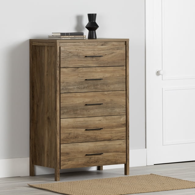 South Shore Gravity 5-Drawer Chest for Adult in natural mango finish with five wide drawers and slim black handles, standing on squared legs on a light wood floor against a white wall, topped with a black vase and books, designed as a tall, space-saving bedroom furniture piece ideal for organizing clothes and accessories in small rooms.