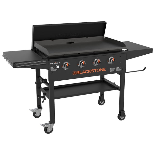 Blackstone 36" Original Griddle with Omnivore Griddle Plate & Flat Top Cover front-facing view of the 36" flat top grill showing the Omnivore griddle plate and hard flat top cover, four independent control knobs for four cooking zones, magnetic utensil retention strip, dual folding side shelves and pivoting paper towel holder, rear grease management tray; 762 square inches cooking surface and 38,000 BTU output per product specs, suitable for outdoor flat-top grilling and often used as a temporary buffet surface for backyard gatherings.