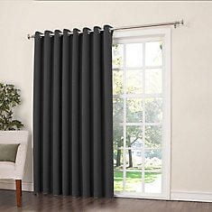 Sun Zero Madrid Patio Door Grommet Curtain in dark charcoal color with grommet top hanging on a metal rod over a sliding glass door, featuring room darkening and energy efficient fabric, set in a bright living room with hardwood floors and a white armchair, ideal for patio doors or large windows.