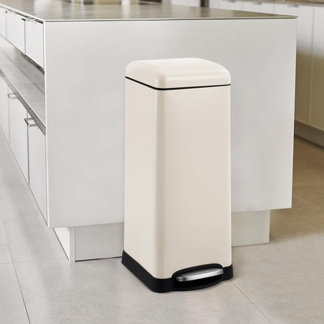 TROPOW 8 Gallon Bathroom Step Trash Can, 30-Liter Square Stainless Steel Foot Pedal Garbage Can with Soft-Close Lid, shown in a beige finish. The trash can features a hands-free foot pedal, a soft-close lid, and a removable inner bucket with metal handles for easy cleaning. Made from durable galvanized steel, it is dent-resistant and suitable for kitchens, bathrooms, and offices. Positioned in a modern kitchen setting with a tiled floor and white cabinetry.