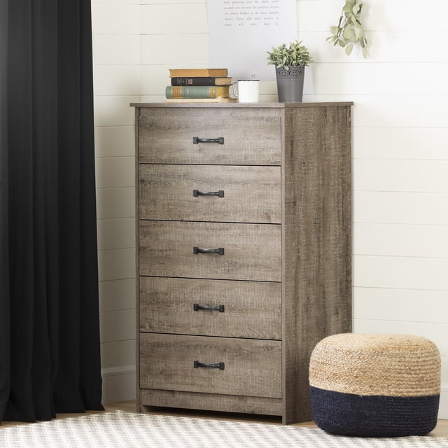 South Shore Tassio 5-Drawer Chest for Adult in weathered oak finish with five drawers featuring black metal handles and metal slides supporting up to 25 pounds each, shown front-facing in a bedroom with white shiplap walls, black curtain, woven pouf, and decorative items including books, a white mug, and a potted plant on top, ideal for organized clothing storage.