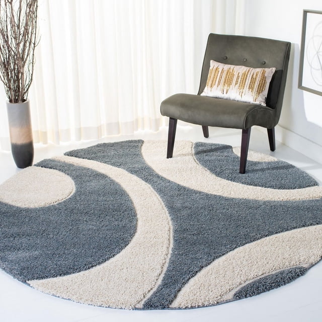 Safavieh Florida Mirabelle Contemporary Shag Area Rug, round with a high-low pile featuring an abstract swirl pattern in grey and crème tones, placed under a dark grey accent chair with wooden legs and a decorative pillow, in a bright room with white curtains and a tall vase with branches, ideal for adding texture and warmth to living areas.