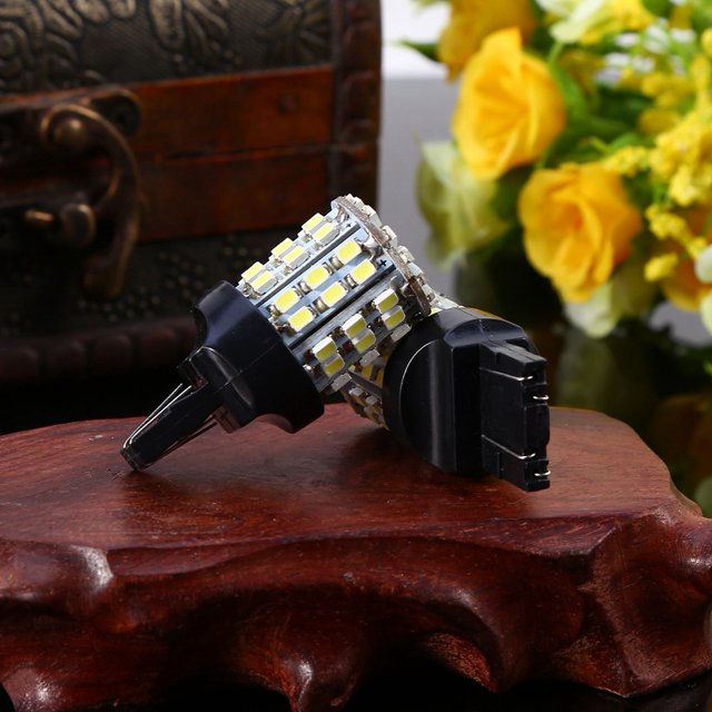 LAFGUR 7443 64-SMD LED Light Bulbs, a set of two white 6000K LED bulbs designed for reverse, brake, stop, and tail lights. Each bulb features 64 high-quality SMD LEDs for enhanced brightness and a wide viewing angle. The bulbs have a T20 socket, operate on 12V DC, and are energy-efficient with no heat output. Displayed on a wooden surface with a decorative background.