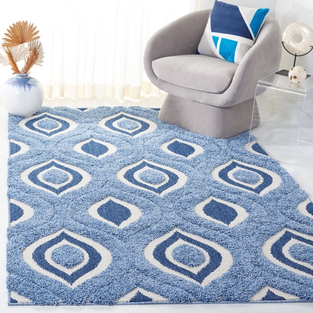 Safavieh Florida Declan Geometric Swirls Shag Area Rug in blue and cream tones with a plush high-low pile emphasizing geometric swirl patterns, placed in a bright room with a gray curved chair featuring a blue and white geometric pillow, a clear acrylic side table, and a white vase with dried palm leaves, suitable for adding texture and comfort to living spaces.