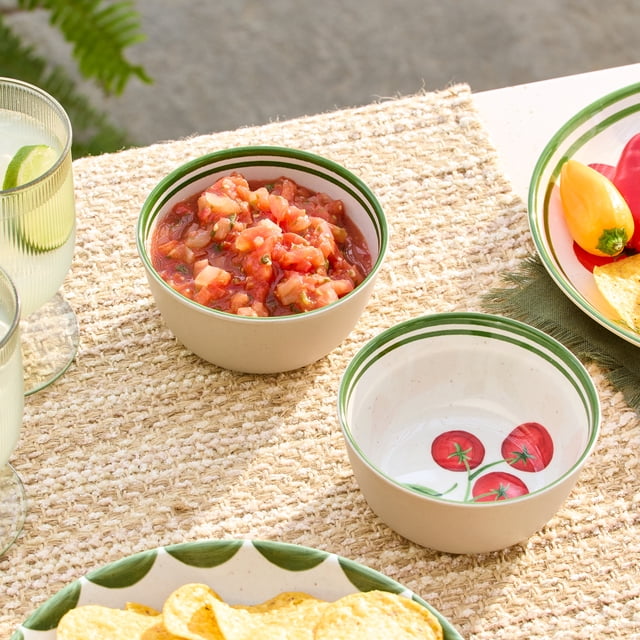 Better Homes & Gardens Bamboo Melamine Dip Bowl 4.65 Inch 2Pc set featuring one bowl filled with salsa and the other empty with a tomato decal inside, both with green rim stripes, placed on a woven placemat with chips and drinks, suitable for serving sauces, condiments, or small snacks during casual dining and entertaining.