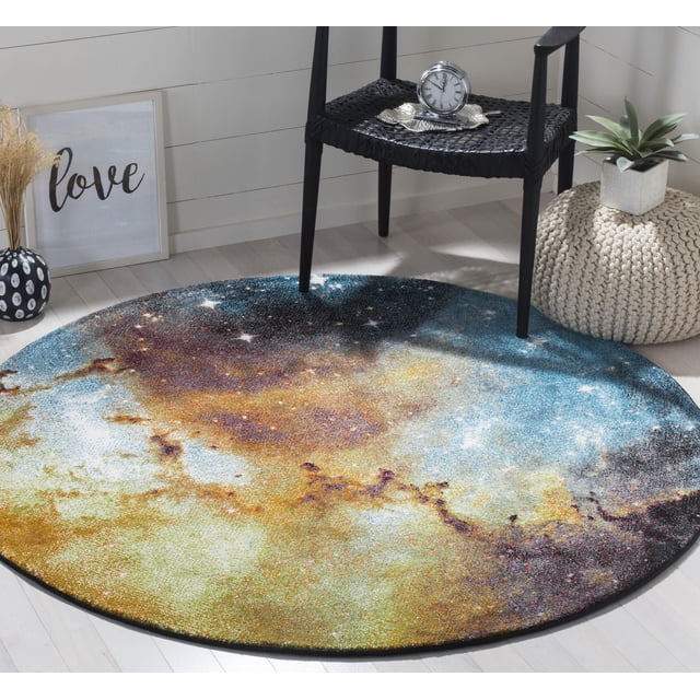 Safavieh Galaxy Kalden Astronomy Area Rug, a round accent rug featuring a celestial abstract pattern in blue, gold, white, and black tones, placed on a light hardwood floor under a black woven chair with a silver clock and beside a beige knitted pouf with a green plant, suitable for contemporary home settings.