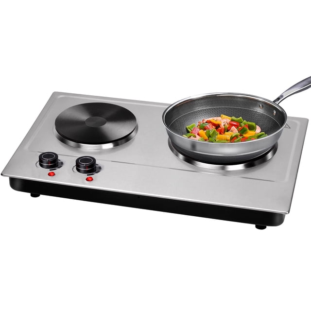 LIVINGbasics 1800W Electric Cooktop Ceramic Hot Plate with dual cast-iron burners, featuring a stainless steel body. The left burner measures 7.4 inches, and the right burner measures 6.1 inches, compatible with various cookware. Includes dual control knobs for temperature adjustment and indicator lights. Shown with a frying pan containing vegetables on the right burner. Compact and portable design suitable for built-in or countertop use.
