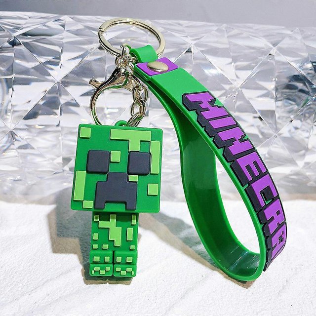 Minecraft Theme Keychain Bag Charm Pendant Key Ring Accessories Stocking Filler Gift featuring a green Creeper character design made of flexible PVC material. Includes a smooth, durable strap with 'Minecraft' text in purple and black, attached to a metal keyring and clasp. Suitable for use as a keychain, bag charm, or decoration for pencil cases and more. Ideal as a gift for fans of the game.