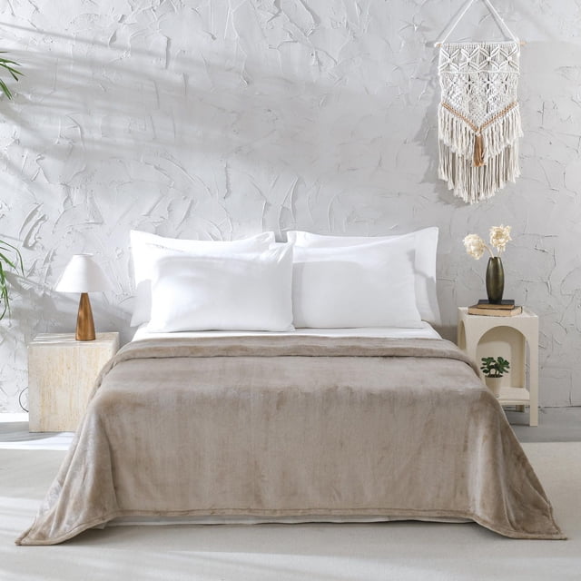 Mainstays Couverture en Peluche Brune DQ Étalée sur un Lit avec des Coussins Blancs dans une Chambre Minimaliste avec un Mur Blanc Texturé et une Suspension Murale en Macramé. la Couverture Douce et Peluche Brune Ajoute une Couche Douillette à la Literie, Assortie à une Lampe en Bois et à une Petite Plante sur les tables d'Appoint, Convient à la Chaleur et au Confort.