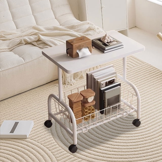 YIMWNYI Rolling Cart Table featuring a compact design with a white wood tabletop and two mesh shelves for storage. The cart is shown in a cozy living room setting, placed on a beige textured rug near a sofa. It is equipped with four black caster wheels for mobility and is styled with books, wooden coasters, and a tissue box. Ideal as a nightstand, mobile coffee table, or versatile storage solution for small spaces like apartments or dorms.