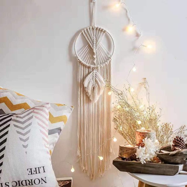 Tree of Life Large Dream Catcher, Macrame Wall Hanging Dreamcatcher displayed in a cozy boho décor setting. The dreamcatcher features intricate handmade macrame patterns with cotton ropes, a circular metal ring, and hanging tassels. It is positioned against a neutral wall, surrounded by decorative elements including pillows with geometric patterns, fairy lights, and a wooden tray with candles and pinecones.