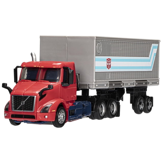Transformers Toys Generations Volvo VNR 300 Optimus Prime 7 Inch Collectible Action Figure showing a front-left angled view of a red and blue Volvo VNR 300 truck cab with a silver trailer featuring blue stripes and the Autobot logo, detailed wheels, side mirrors, and realistic truck features, suitable for display or play.