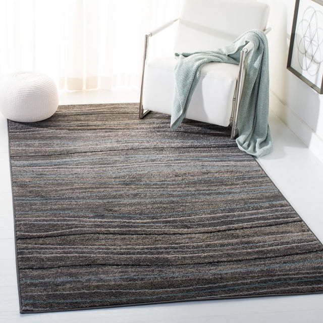 SAFAVIEH Amsterdam Aragon Striped Area Rug featuring horizontal stripes in gray and blue earth tones, power loomed from durable synthetic yarns. Positioned on a light floor next to a white armchair with a light blue knitted throw and a white knitted pouf, ideal for rustic-chic accent décor.