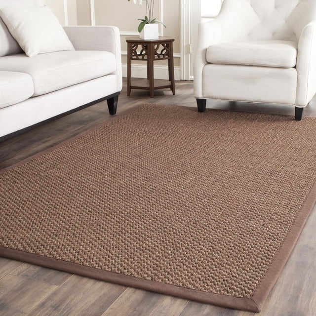 Safavieh Natural Fiber Charlene Braided Area Rug in marble, 8' x 11', displayed on wood flooring between a cream sofa and tufted armchair, featuring a textured braided sisal surface with a fabric border, ideal for coastal or casual living rooms.