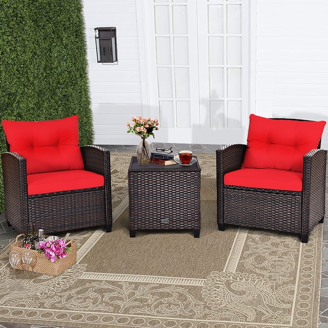 Costway 3PCS Patio Rattan Furniture Set Cushioned Conversation Set Sofa Coffee Table Red. This outdoor furniture set includes two single chairs with red cushions and a square coffee table with a tempered glass top. Constructed with a sturdy steel frame and hand-woven rattan in a mix brown color, it is suitable for patios, gardens, or poolside areas. The chairs feature wide armrests and thick cushions with removable, washable covers for added convenience. The coffee table offers a stable surface for drinks, snacks, or decor. The set is shown on a decorative outdoor rug in front of a white wall with greenery.