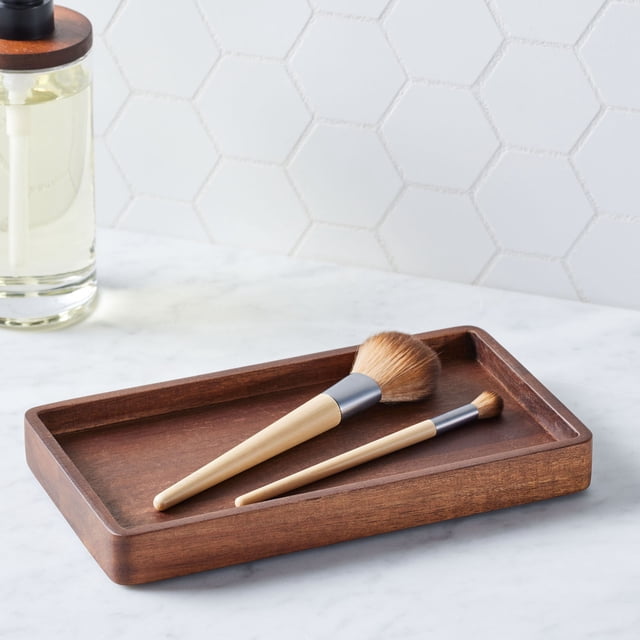 Better Homes & Gardens Acacia Wood Tray Organizer in walnut finish, rectangular with raised edges, holding two wooden-handled makeup brushes on a white marble countertop with white hexagonal tile backsplash, ideal for organizing cosmetics or jewelry and suitable as a decorative display in bedrooms or living spaces.