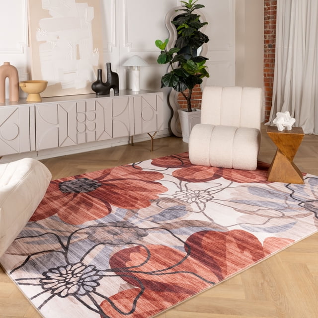 Rug Branch Modern Floral Indoor Area Rug measuring 6'7" x 9'6" with large red and muted purple floral patterns on a cream background, placed on light wood parquet flooring in a modern living room with a white boucle lounge chair, wooden geometric side table, decorative console, and potted plant.