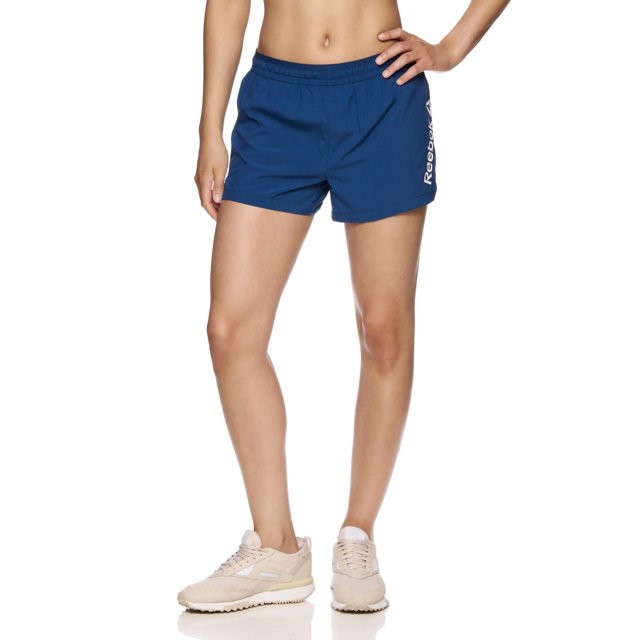 Reebok Women's Staple Running Short with Mesh Lining in blue, front view on a model, featuring elastic waistband with inside drawcord, side slit, breathable mesh lining, and white Reebok Delta logo on left leg, made of lightweight polyester, ideal for running and training.