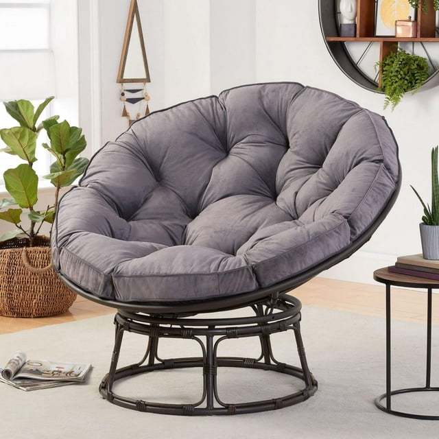 Better Homes & Gardens Emma Papasan Accent Chair with a 53.5-inch diameter tufted gray cushion on a dark brown faux wicker steel frame base, suitable for living room seating and accent decor, shown in a bright room with plants and a side table.
