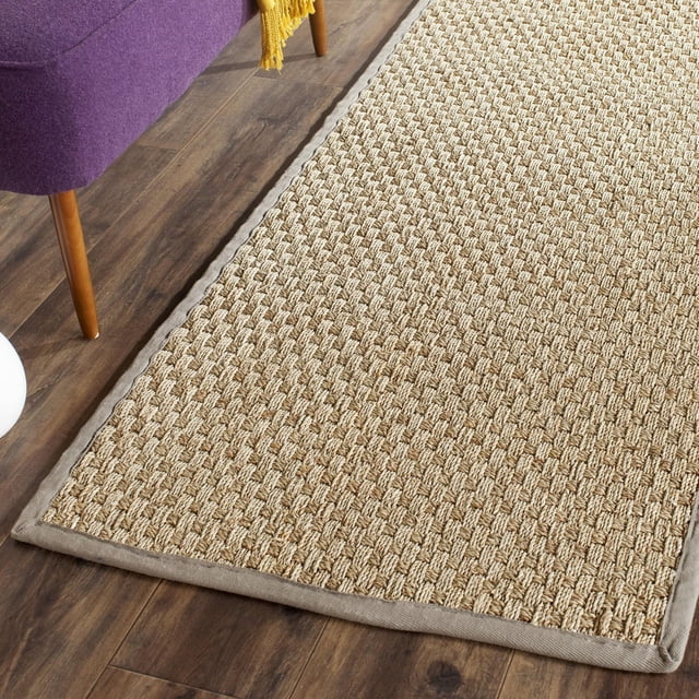 Safavieh Natural Fiber Arbor Border Area Rug with woven sisal texture in natural beige and a durable fabric border, placed on dark hardwood flooring beside a purple chair with wooden legs and a yellow throw, ideal for coastal or casual interiors.