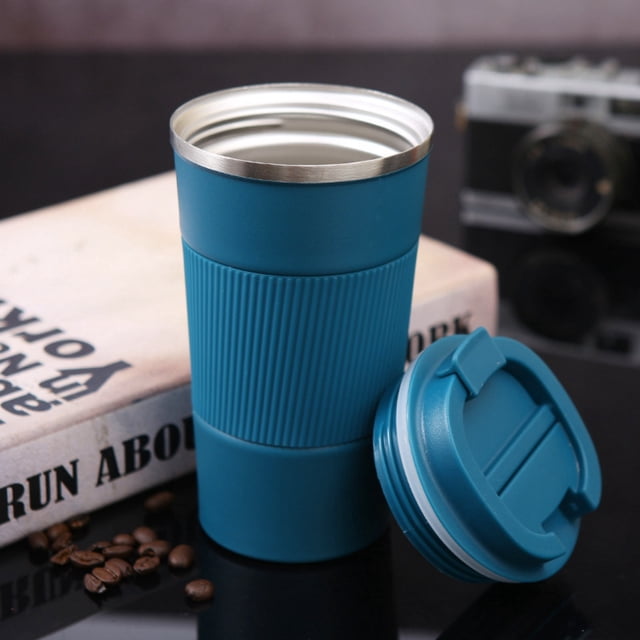 Ganfancp Tasses à Café de Voyage 17oz Tasse Isolée Gobelet Thermique à Emporter avec Couvercle Étanche Réutilisable Tasse à Café en Acier Inoxydable Anti-Fuite pour Boissons Chaudes et Froides Glacées (Noir, 510ml). l'Image Montre une Tasse de Voyage en Acier Inoxydable Bleue avec un Manchon en silicone Côtelé pour la Prise, une Grand Ouverture, et un Couvercle Amovible Placé à Côté. la Tasse Est Affichée sur une surface Noire avec des Grains de Café et un Livre en Arrière-Plan.