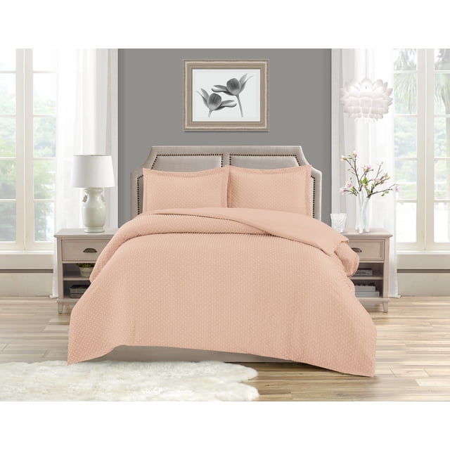 Swift Home Dot Clip Textured Duvet Cover Set king size in soft pink with a raised dot pattern, including duvet cover and two pillow shams. Shown on a beige upholstered bed with nailhead trim in a bright room with wood flooring and neutral walls. Features a hidden zipper closure and breathable fabric for all-season comfort, ideal for adding subtle texture to bedroom décor.