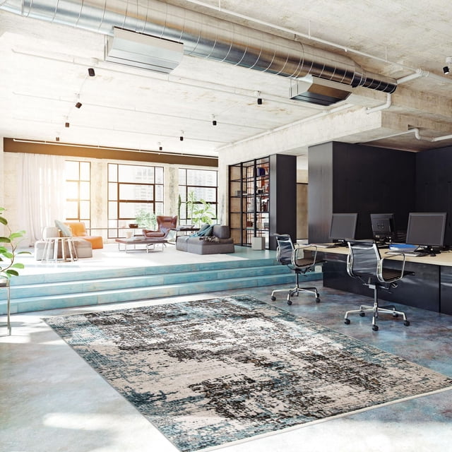 ECARPET Tapis Moderne Abstrait Collection Sparrow dans un Bureau Industriel Lumineux avec Planchers en Béton et Conduits Exposés. le Tapis d'Accent Présente un style Transitionnel Motif Abstrait dans des Tons Bleu, Gris et beige, Placé Près d'Une Aire d'Assise Surélevée avec des Meubles Modernes et de Grandes Fenêtres. Idéal pour les Zones à Fort Passage et les Bureaux à Domicile.