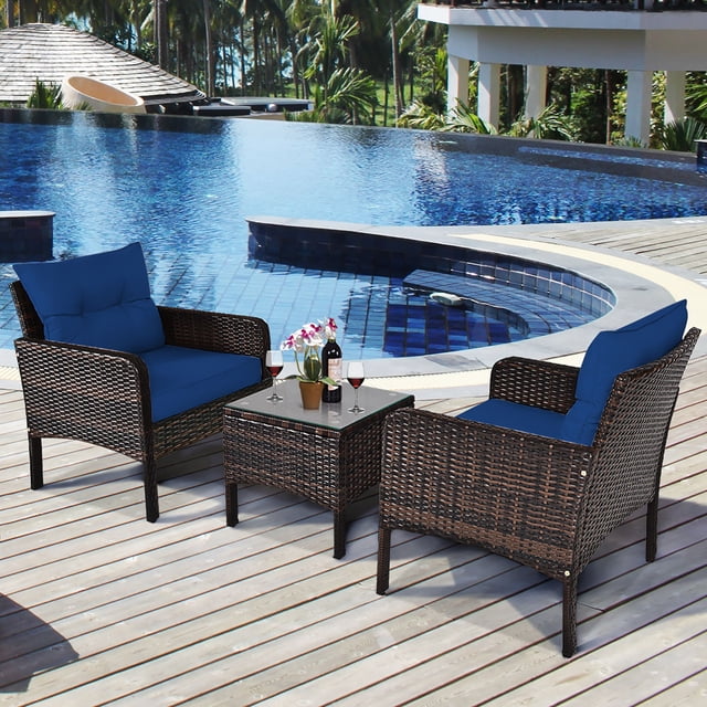 Costway 3PCS Outdoor Rattan Conversation Set Patio Garden Cushioned Sofa Chair Navy. This set features two black PE rattan chairs with navy blue cushions and a coffee table with a tempered glass top. The furniture is displayed on a wooden deck near a pool, ideal for patios, balconies, or gardens.