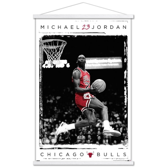 Michael Jordan - Dunk Wall Poster, 14.725" x 22.375" framed showing Michael Jordan in a red Chicago Bulls jersey number 23 jumping mid-air for a basketball dunk, holding the ball in his right hand, wearing white Nike sneakers, set against a black and white crowd background, with 'MICHAEL 23 JORDAN' text above and 'CHICAGO BULLS' with the team logo below, suitable for sports-themed room decor.