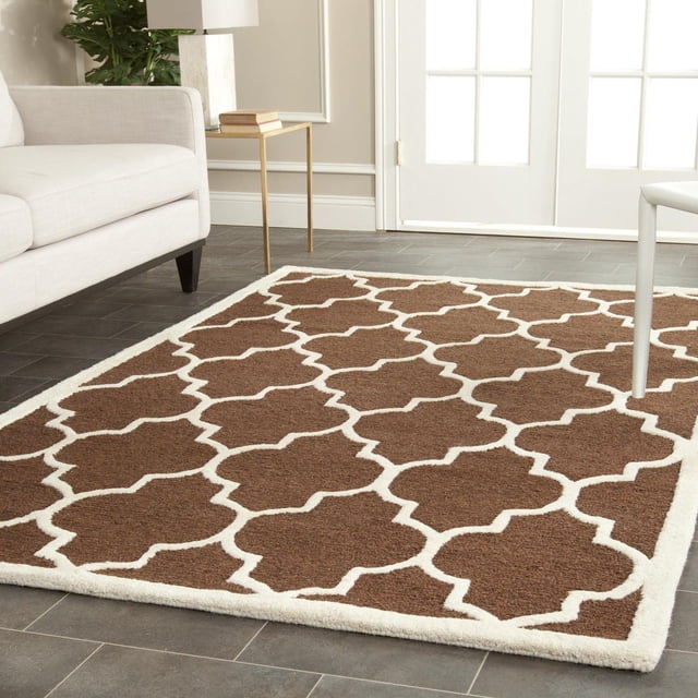 Safavieh Cambridge Kevin Geometric Area Rug with brown and white geometric trellis pattern in plush cut pile wool, placed on dark tile flooring in a modern living room with beige sofa and gold side table, ideal for adding classic American style to home or office decor.