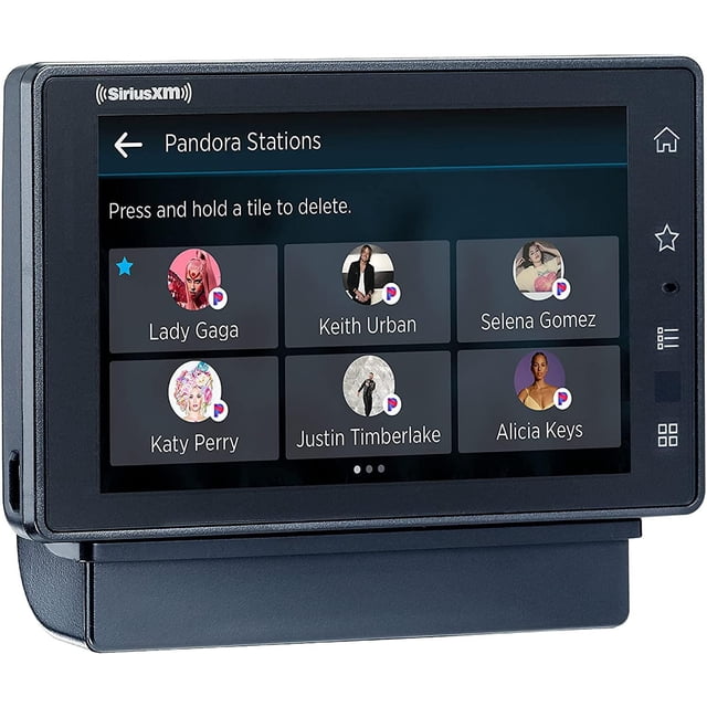 SiriusXM Tour Satellite Radio with Vehicle Kit displaying a front-facing touchscreen showing Pandora Stations interface with artist tiles for Lady Gaga, Keith Urban, Selena Gomez, Katy Perry, Justin Timberlake, and Alicia Keys, set in a black frame with side buttons for tuning and menu control.
