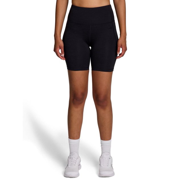 Reebok Short Taille Haute Reflex pour Femmes en Noir, Vue avant d'Un Modèle Debout sur Fond Blanc, avec une Taille Haute Ajustée, des Poches Latérales, un Tissu polyester-spandex Évacuant l'Humidité et un Petit logo Reebok sur la Jambe Gauche, Idéal pour l'Entraînement Ou les Tenues Décontractées.