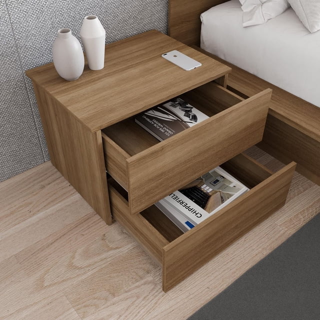 Nexera James Nightstand with 2 Drawers in rich oak finish, shown from a 3/4 front angle with both drawers open containing books. This Scandinavian bedroom furniture piece sits beside a bed with white linens on a light wood floor and textured grey wall. Its compact design offers convenient storage for bedside essentials and is often used as a small workspace or charging station.