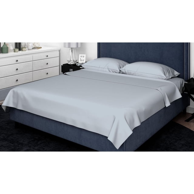 Johnson Home 600 Thread Count Organic Cotton Sheet Set in light grey on a navy upholstered bed with nailhead trim, including two pillowcases, in a modern bedroom with white dresser and glass lamp on a black nightstand, offering breathable, soft, and durable bedding suitable for year-round use.
