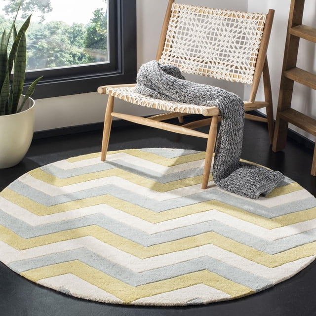 Safavieh Chatham Jake Tapis à Rayures Zigzag Est un Tapis Rond en Laine Tufté à la Main avec une Hauteur de Poil Moyenne, Présentant des Rayures Zigzag Jaune, Gris Pâle et Blanc Cassé, Placé sur un Plancher Sombre sous une Chaise en Bois Tressée avec un Jeté Tricoté Gris, Près d'Une Fenêtre et d'Une Plante Serpent en Pot, Convenant pour Ajouter Douceur et style à la Déco Contemporaine de la Maison.