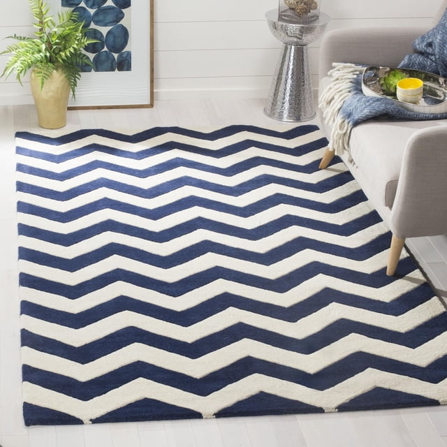 Safavieh Chatham Jake Tapis à Rayures Zigzag avec Motif Zigzag Bleu Marine et Blanc, construction en Laine Tuftée à la Main et Hauteur de Poil Moyenne pour Plus de Douceur, Placé sur un Plancher de Bois Franc Clair à Côté d'Un sofa beige, table d'Appoint Argentée et Jardinière Dorée avec Fougère Verte, Convient comme Tapis d'Accent durable pour les Espaces de Vie Contemporains.