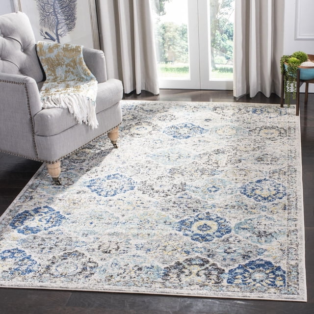 SAFAVIEH Madison Tapis Géométrique Floral Judith Présentant une Forme Rectangulaire avec un Motif Floral et Géométrique Usé en Tons Bleu, Gris et Crème. Tissé Mécaniquement pour la Durabilité, Il Est Montré sur un Plancher de Bois Franc Foncé à Côté d'Un Fauteuil Gris avec un Jeté à Franges, Idéal pour Ajouter du style et du Confort aux Espaces de Vie Contemporains et Transitionnels.