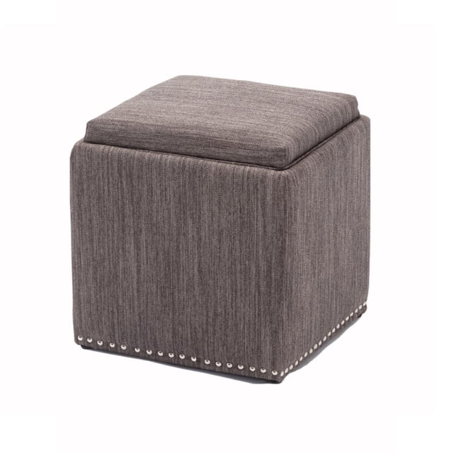 Chase Fabric Ottoman With Flip Tray Lid in charcoal gray, shown in a 3/4 view. This cube ottoman features textured gray fabric upholstery, a padded reversible tray lid, and silver nailhead trim along the base. Measuring 18L x 18W x 18H inches, it offers storage and functions as a footstool, coffee table, or storage bench, suitable for living rooms or bedrooms.