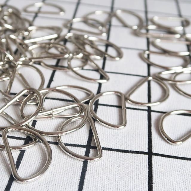 SHOWERORO Multipurpose D Rings 20Pcs Metal for DIY Crafts and Pet Owners. A close-up view of silver metal D rings with a semi-circular design, scattered on a grid-patterned surface. Perfect for jewelry findings, jump rings, crafting handbags, belts, dog collars, and luggage accessories, featuring an anti-skid design for secure fastening.